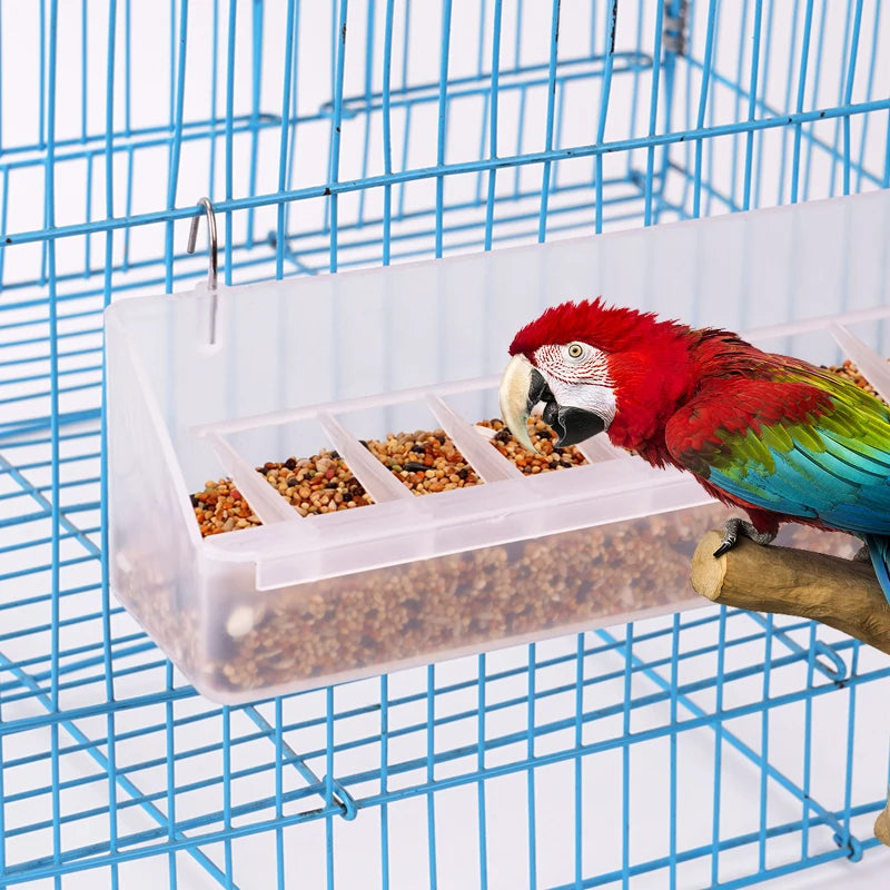 A red macaw is feeding from a clear plastic bird feeder and waterer inside a blue wire cage.