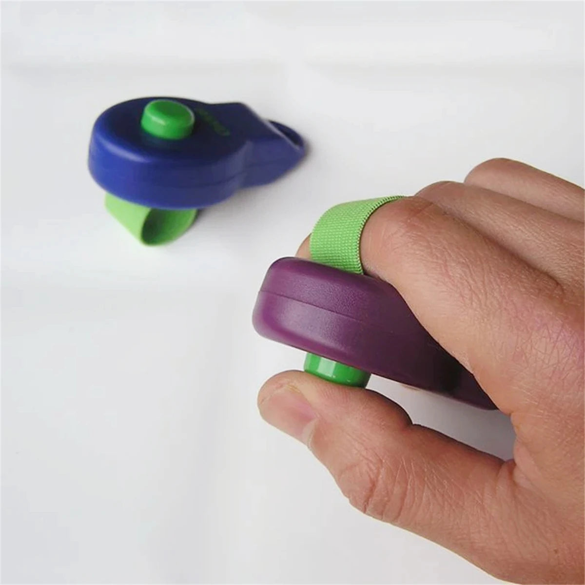 A hand holds a purple dog training clicker with a green finger band.