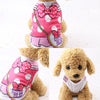 Un chien duveteux portant un gilet à pois rose et blanc avec un nœud rose et un collier en chaîne dorée.