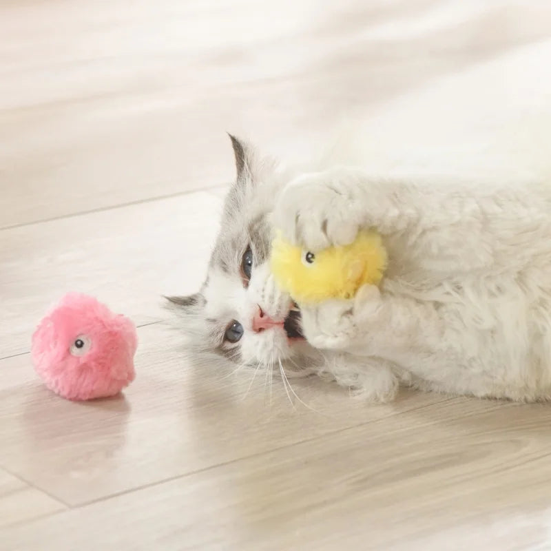 Ein flauschiger weißer Kater interagiert mit einem rosa Plüschball und einem gelben Plüschspielzeug.