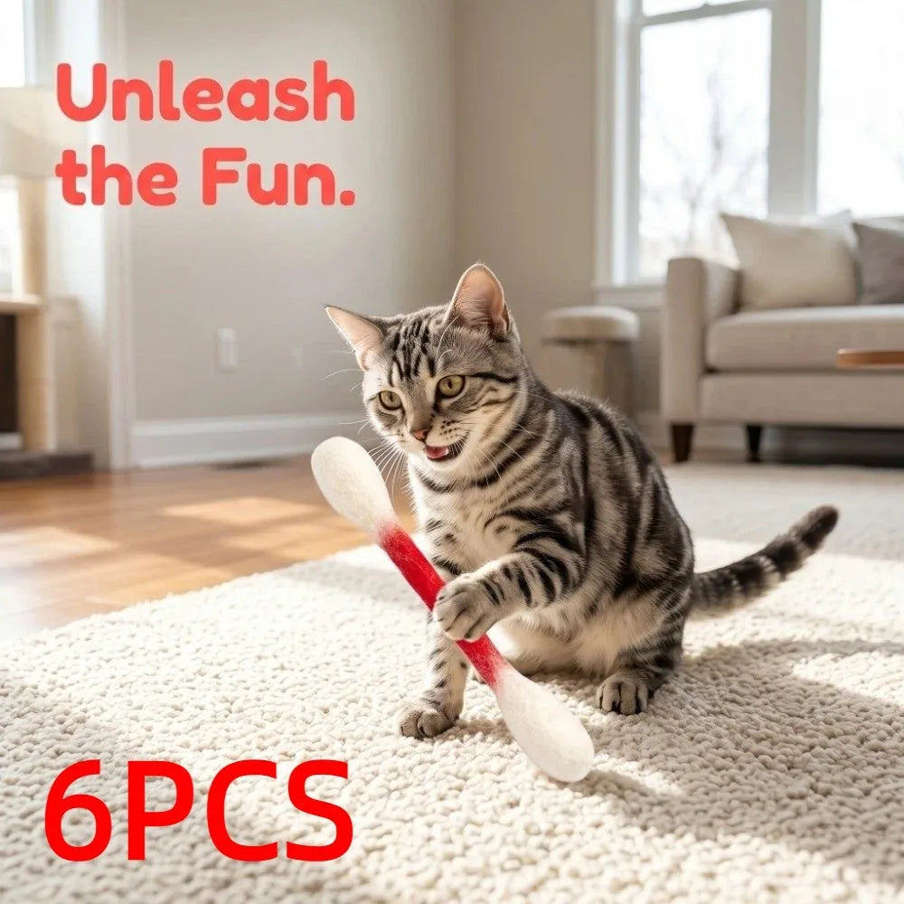 A tabby cat is playing with six white cotton swab toys on a white rug indoors.