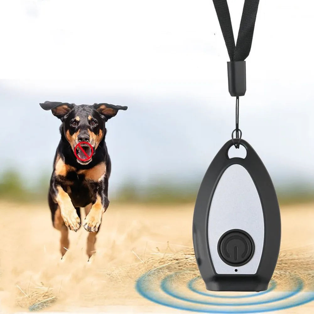 A black and brown dog is jumping in the air next to a handheld ultrasonic dog bark deterrent device on a sandy surface.