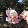 Ein flauschiger weißer Hund mit einem rosa Herzmuster-Teddy-Hoodie sitzt auf einem Metallstuhl im Freien.