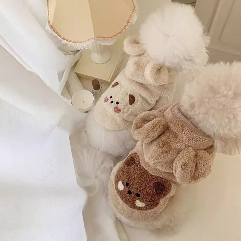 Un pull en polaire polaire pour chien, brun clair avec bordure blanche duveteuse, posé sur une surface blanche.