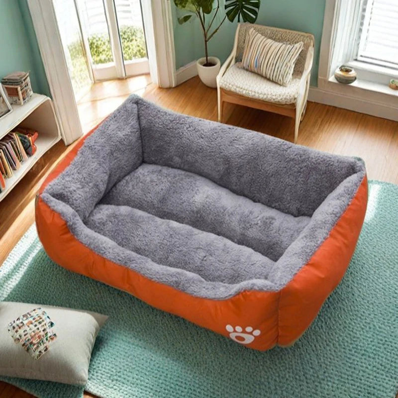 A gray and orange plush dog bed is placed on a mint green rug in a bright room.