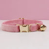 A pink velvet cat collar with a gold-tone buckle and a small gold bell.