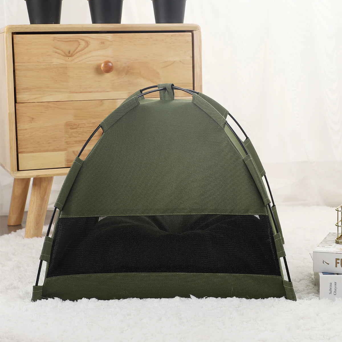 Un lit pour chat confortable en olive foncé est exposé sur une surface blanche et duveteuse à côté d'une commode en bois.