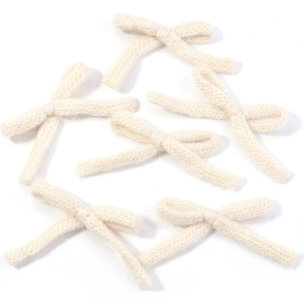 A set of six handmade knitted cotton bows in a light cream color