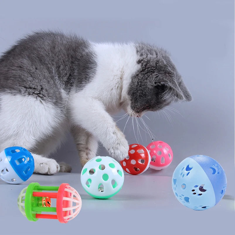 A gray and white cat is interacting with a set of ten colorful plastic toy balls, including blue, red, and green ones.