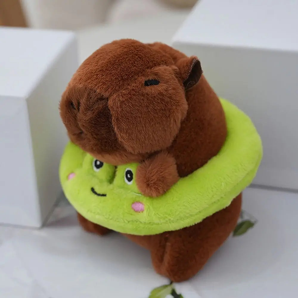 Braune Capybara-Plüschpuppe mit limettengrüner Kapuzenjacke und Flügel, auf weißer Oberfläche.