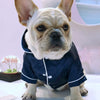 A fawn-colored dog wearing a dark blue silk pajama top with white trim.
