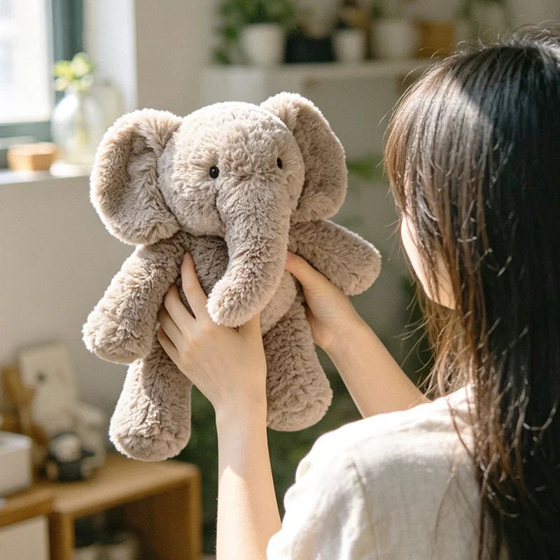 A person is holding a light brown elephant plush toy with its arms stretched out, indoors.