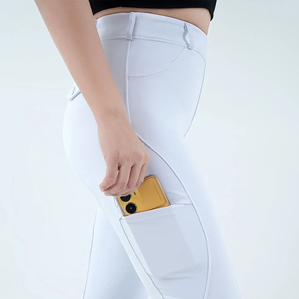A hand is inserting a gold smartphone into the pocket of white riding breeches.
