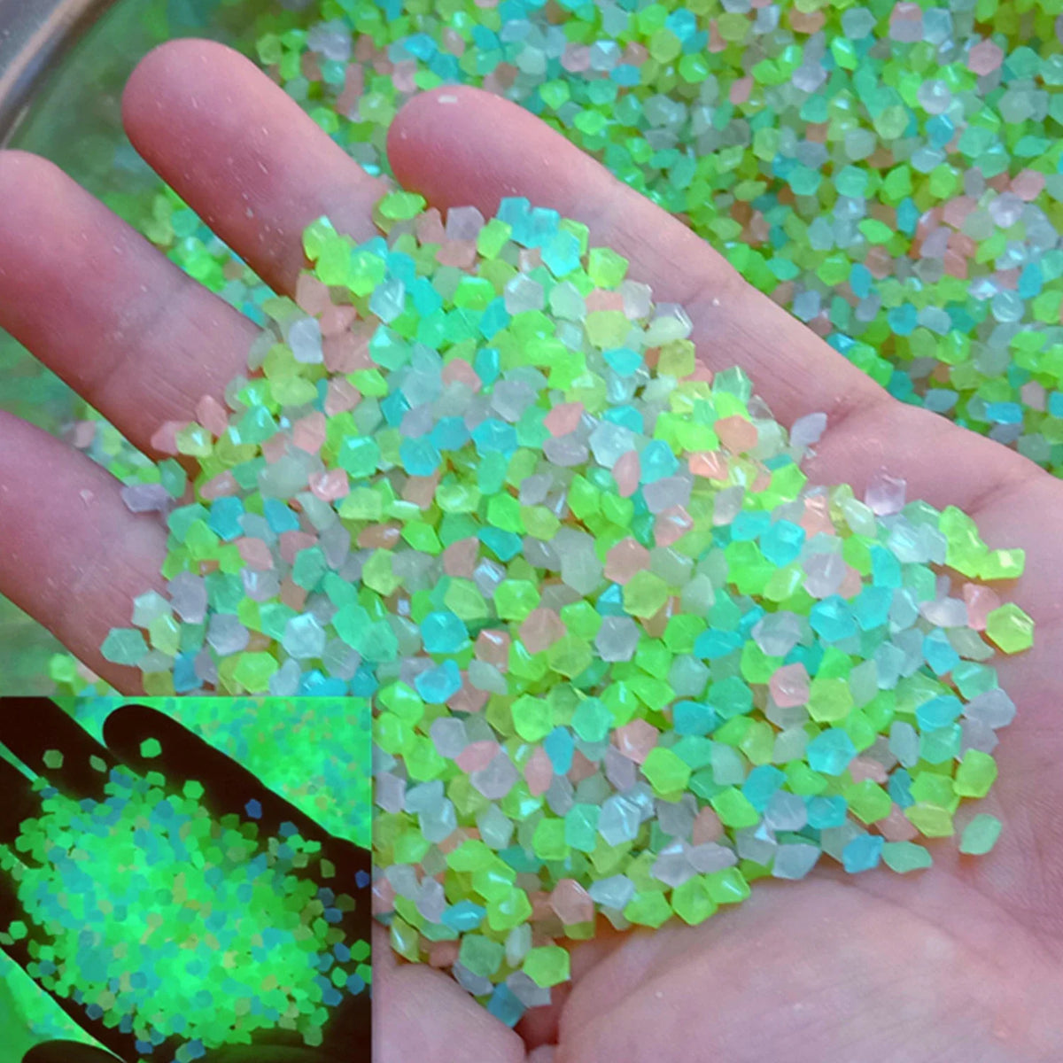 A hand holds a pile of glow-in-the-dark decorative resin pebbles in various shades of green and pink.