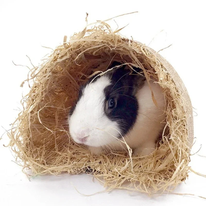 A small white and black pet is nestled inside a natural grass tunnel hideout for small pets.