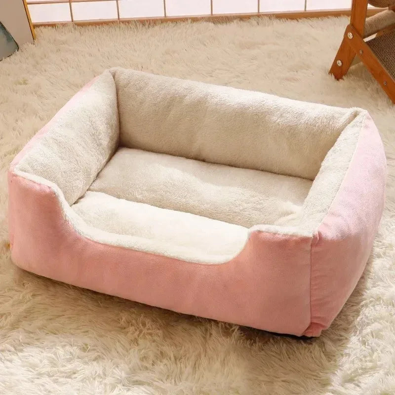 Un coussin de lit pour chat rose et crème posé sur un tapis blanc moelleux.