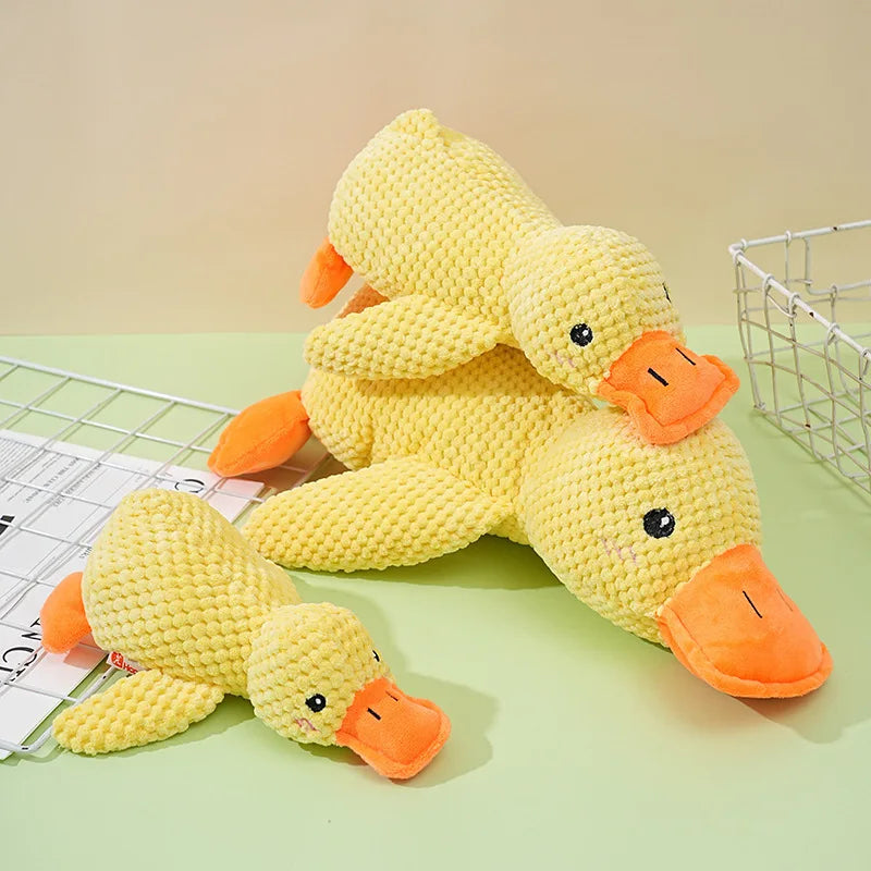 A yellow crocheted plush duck toy with orange feet and beak lying on a light green surface.