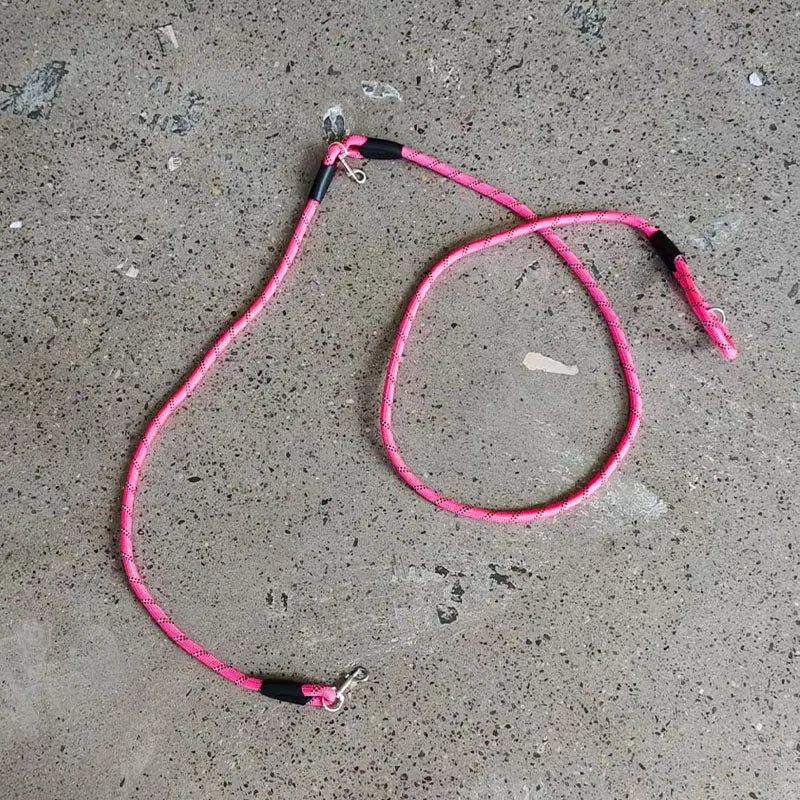 A pink hands-free dog leash with a reflective stripe lying on a gray concrete surface.