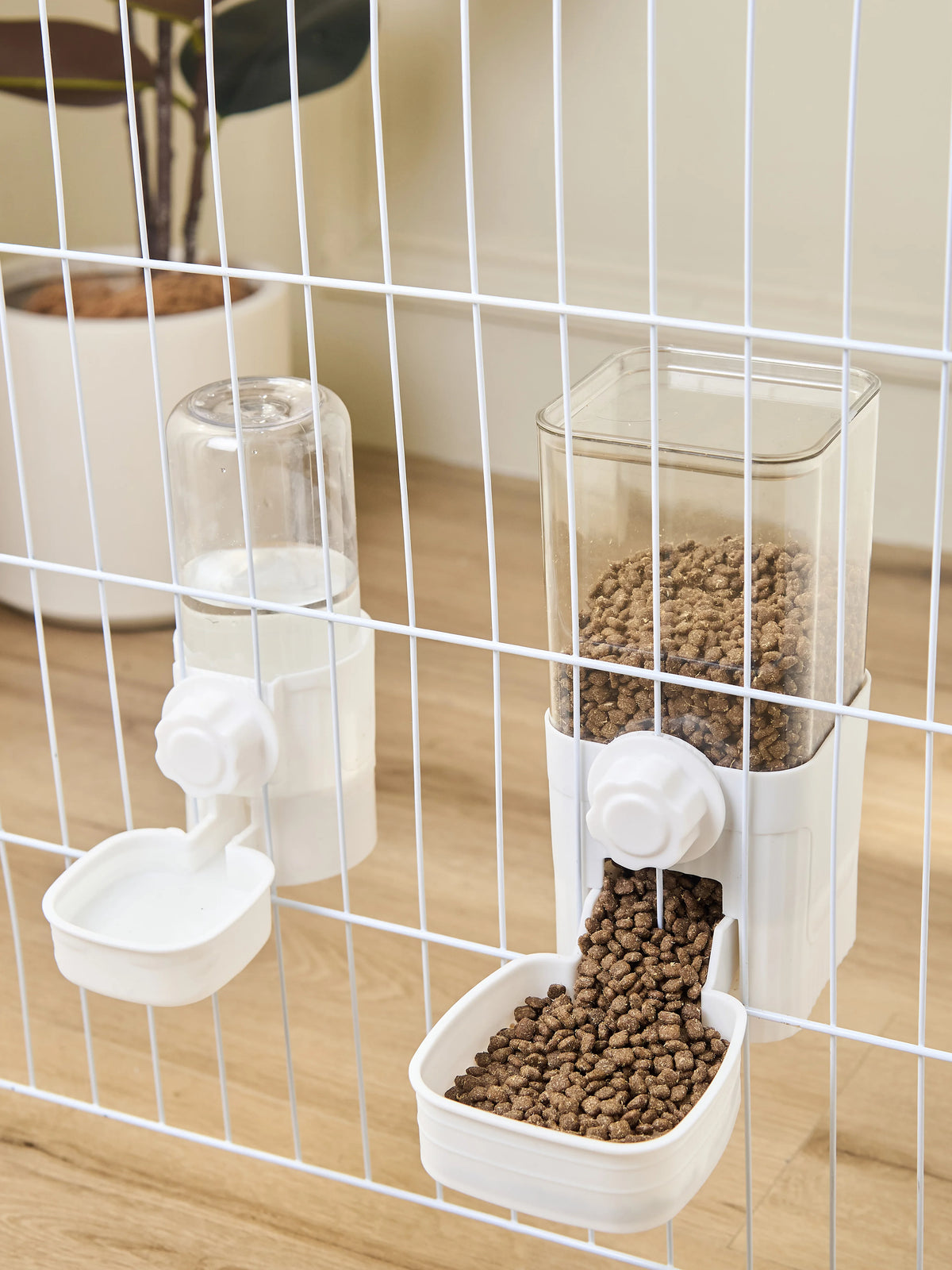 A white automatic pet feeder containing dry food and a separate compartment for water, viewed through a wire mesh cage.