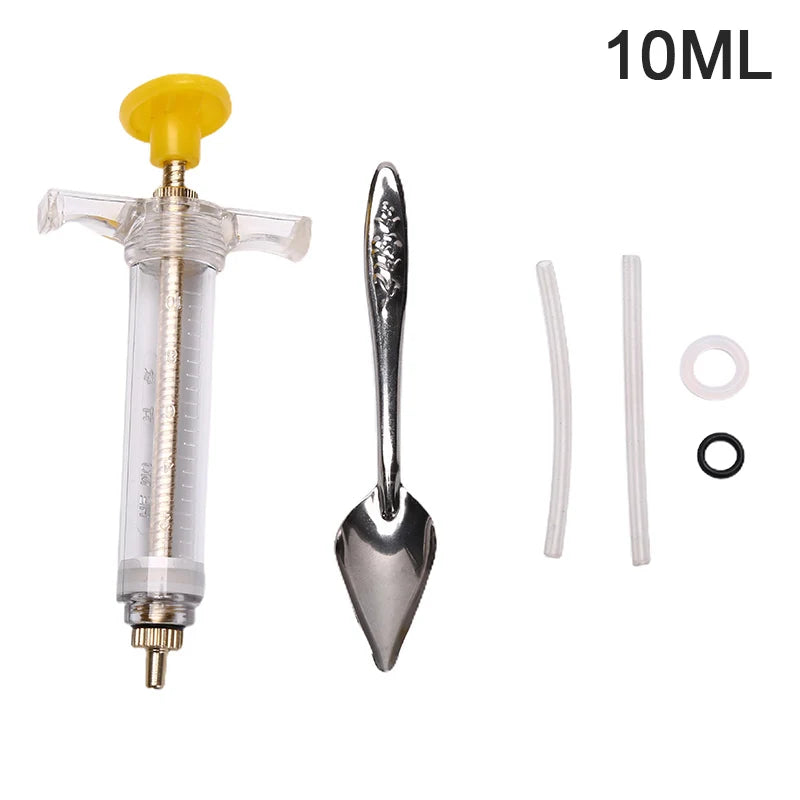 A clear plastic syringe with a yellow plunger and a metal feeding spoon attached, used for parrot feeding.