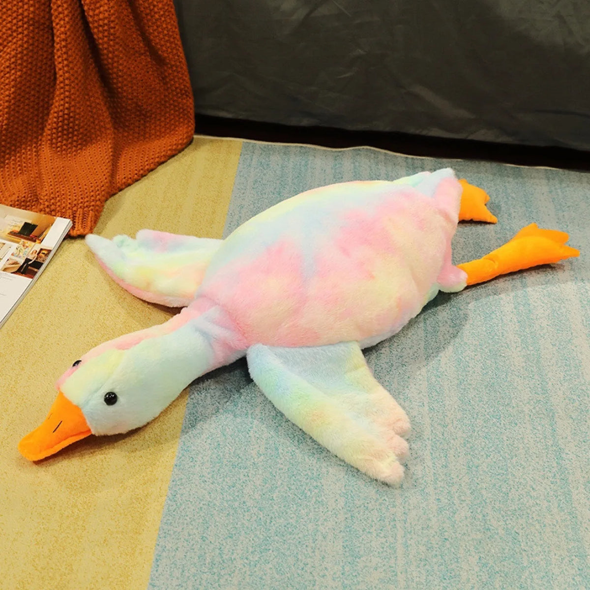 A soft plush duck toy with pink and yellow coloring is lying on a light blue surface.