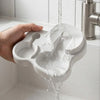 A hand pours white powder into a 2-in-1 mushroom cat feeder and water dispenser placed in a sink.