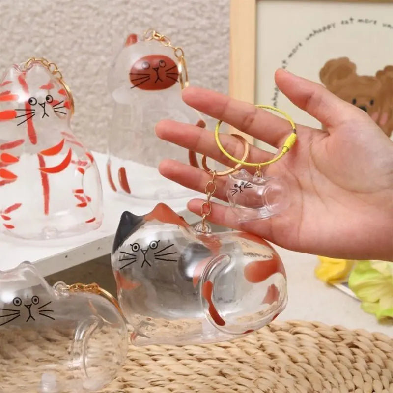 Eine Hand hält eine Set klarer Glaskatzenfiguren mit goldfarbenen Ringen, als Schlüsselanhänger für Paare.