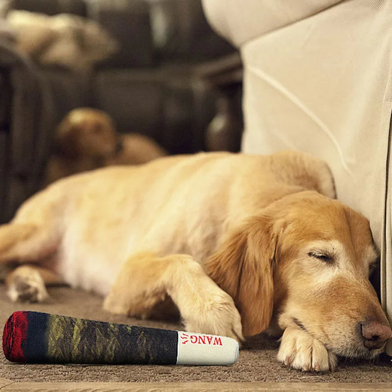 A golden retriever puppy is lying down next to a rolled-up plush dog toy on a brown surface.