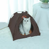 A brown foldable outdoor cat tent with an entrance showing a white cat inside on a white fluffy surface.