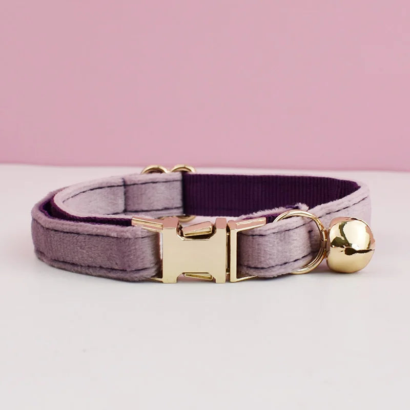 A purple velvet cat collar with a gold-toned buckle and a spherical bell.