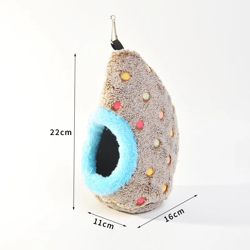 A fluffy, beige bird nest shaped like a teardrop is shown hanging by a loop, with a bright blue entrance.