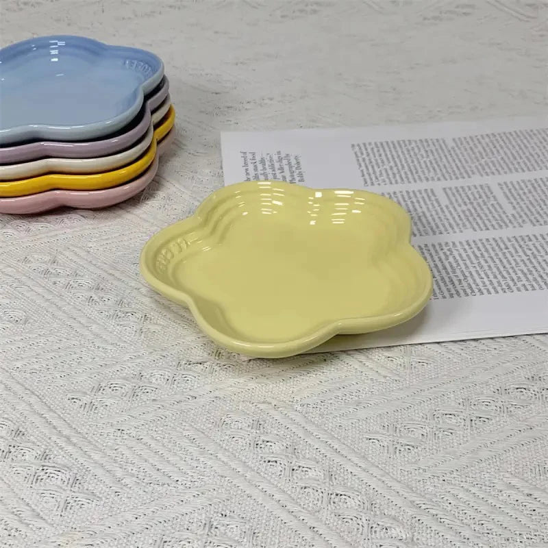 A yellow flower-shaped ceramic pet bowl and dipping dish is shown next to a stack of colorful ceramic dishes.