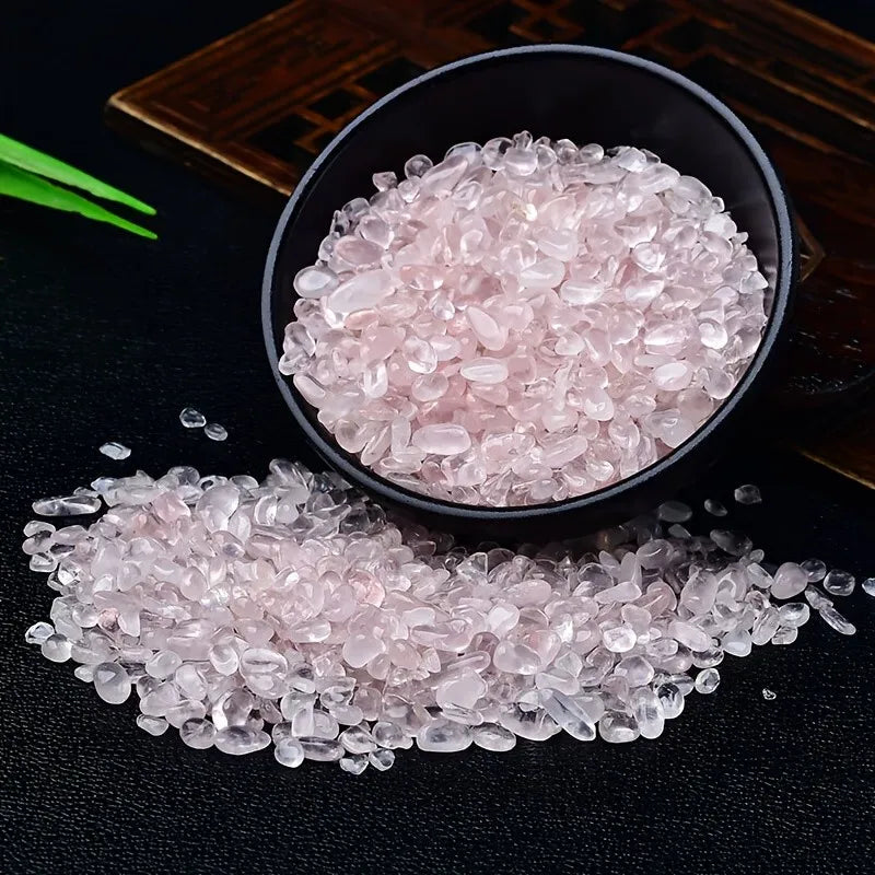 Pink rose quartz crystal chips scattered on a dark surface and in a black bowl.