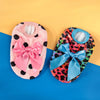 A pink fuzzy knit pet sweater with a pink bow and black polka dots next to a blue and leopard print sweater with a blue bow.