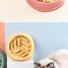 A fluffy white cat is eating food from a pink bowl, with other blue and gold bowls visible.