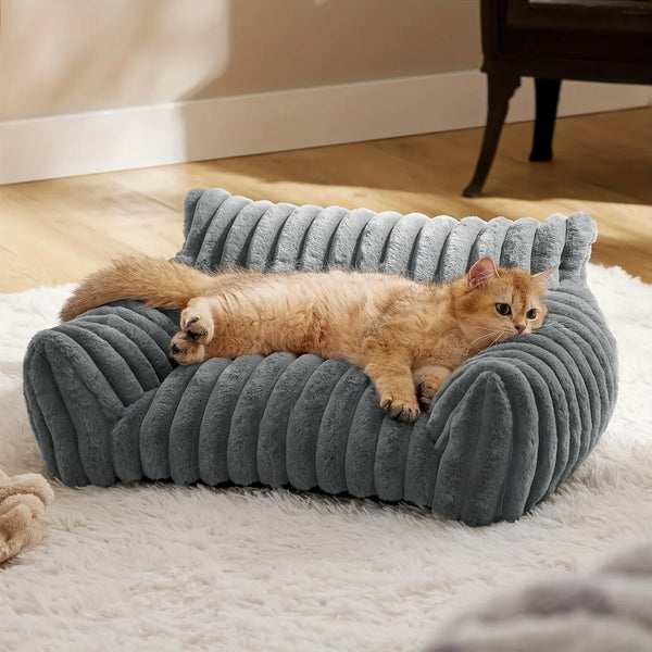Ein flauschiger, orange Kater entspannt sich in einem grauen, gerippten Plüschkratzbaum auf einem weißen Teppich.