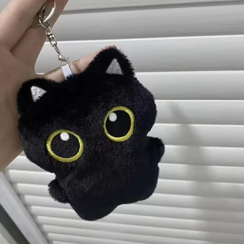 A black cat plush pendant with large yellow eyes is attached to a silver keychain ring.