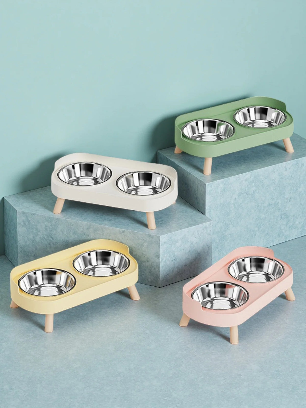 A set of three elevated pet feeders with dual stainless steel bowls in light green, cream, and pink tones.