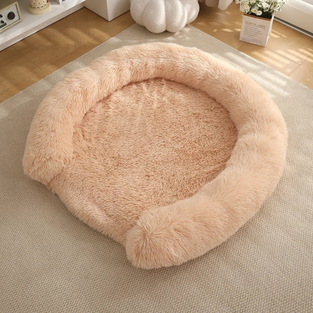 A round, fluffy, light pink dog bed with a removable cover resting on a beige carpet.