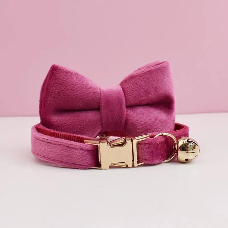 A pink velvet cat collar with a bow and a gold-toned buckle and bell.