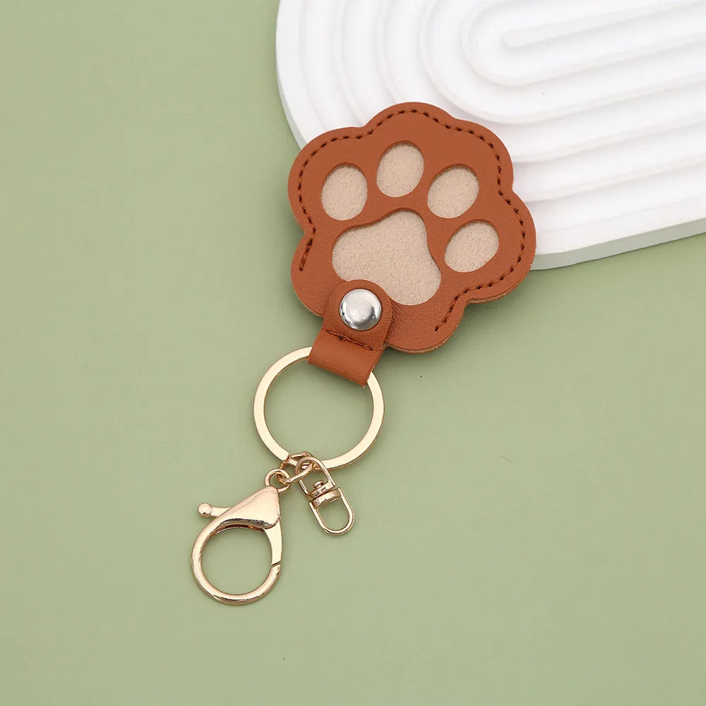 A brown leather paw print charm attached to a gold-colored keyring.