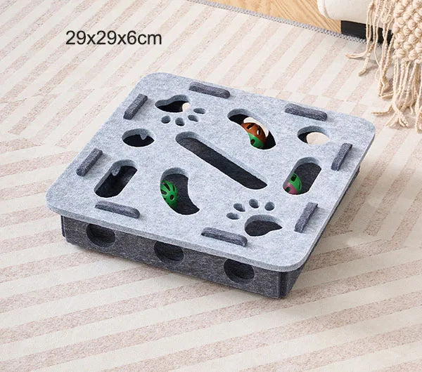 Puzzle en forme de labyrinthe de chat en feutre gris avec des trous et une cloche sur un tissu clair.