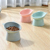 Three ceramic pet feeding bowls in pink and mint green colors resting on a light wooden floor.