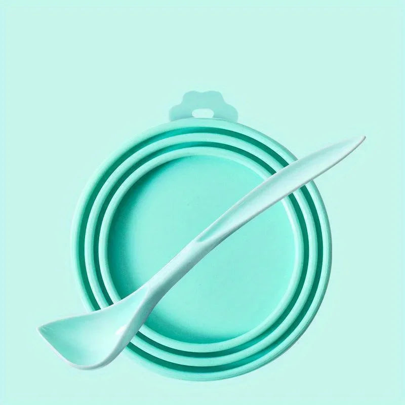 A teal pet food can lid and spoon set resting on a light mint green background.