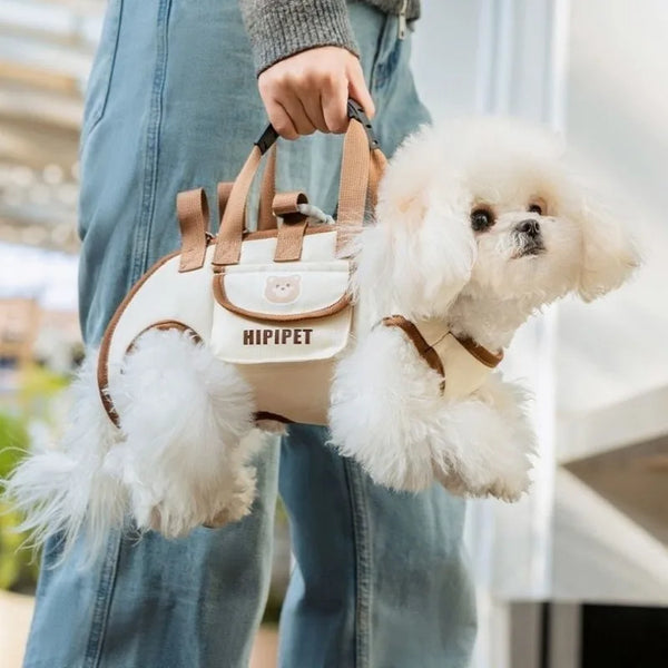 A person holds a beige dog carrier bag with brown straps and white fluffy dog in a light setting.