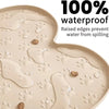 A beige silicone pet feeding mat showing water droplets on its surface with raised edges.