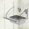A stainless steel pet feeding bowl is suspended by a wire and mounted on a white grid structure.