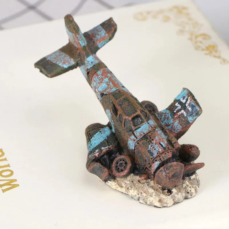 Modelo de avión de resina en tonos azules y marrones desgastados, exhibido sobre una pequeña roca.