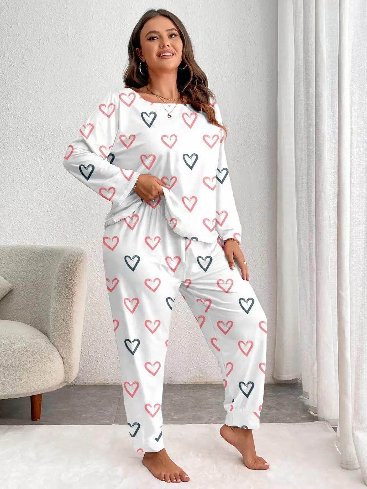A woman models a white pajama set with a repeating pattern of small heart prints on the chest and legs.