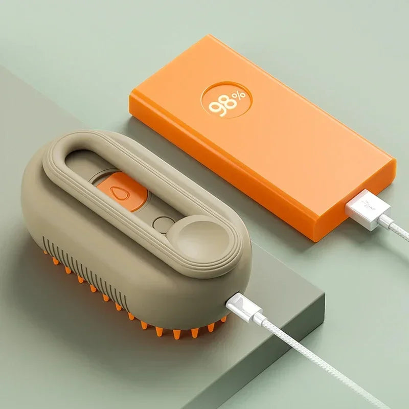 An orange box and a beige pet grooming brush with a steam spray attachment are shown on a light green surface.